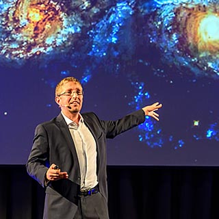 Vortragsfoto: Florian Aigner vor Galaxie-Hintergrund
